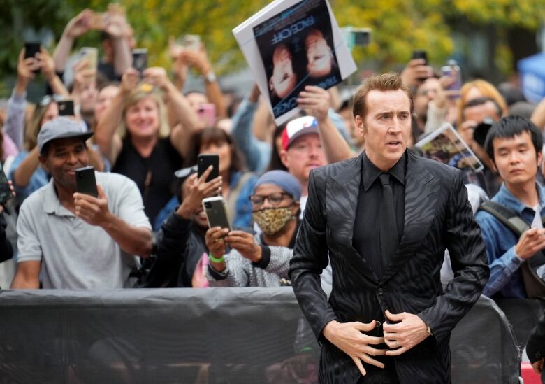 Actor wearing black animal print jacket stands in front of a line of fans during TIFF.