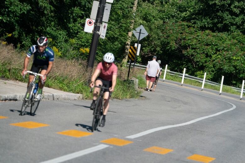 Cyclists and pedestrians on the shoulder of a steep road.