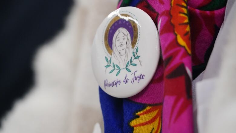 close up of a pin on a scarf. The pin has the logo of Joyce's Principle which is a drawing of Joyce Echaquan's face.