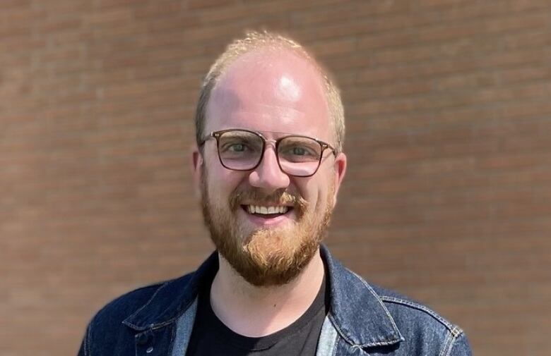 A man with glasses, wearing a denim jacket. 