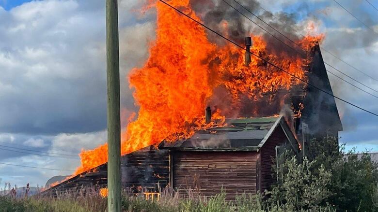 An old wooden building on a rural lot is consumed by flames.