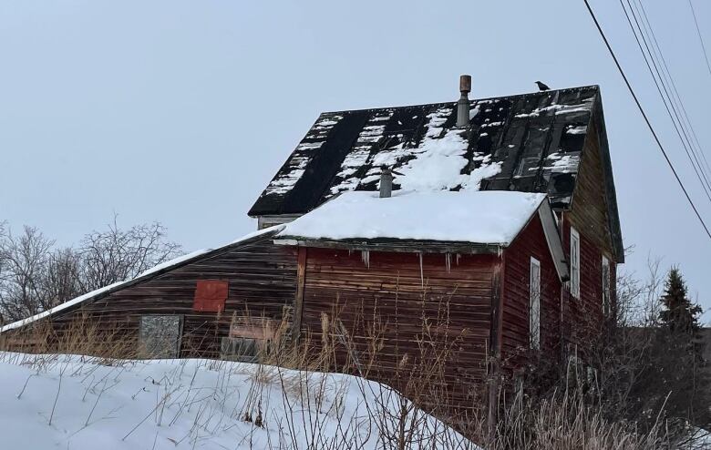 An old wooden building on a rural lot is seen on a snowy day.