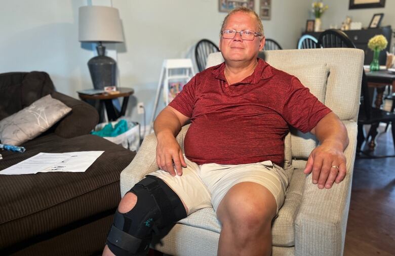 A man with a brace around his knee sits in a reclining chair in his home.