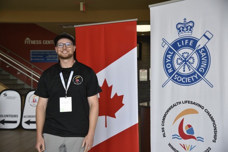 A man in a black shirt stands in front of a banner and a Canadian flag. 