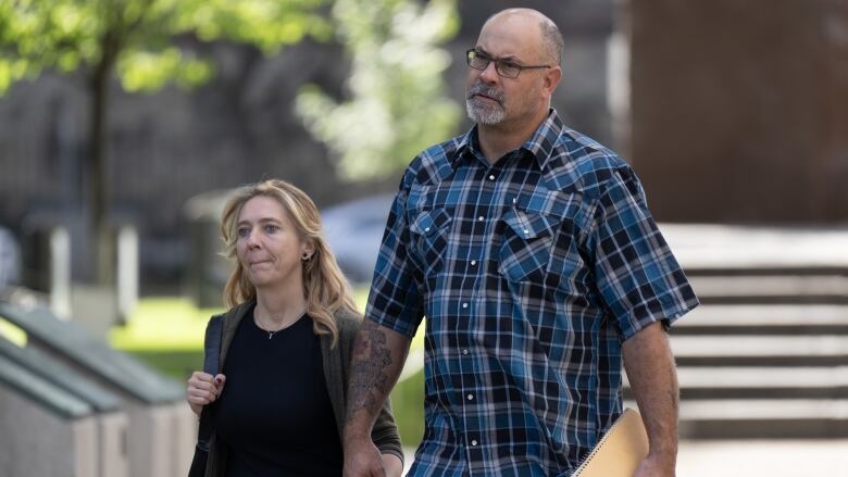 A man and woman hold hands as they walk toward a courthouse on a summer morning.