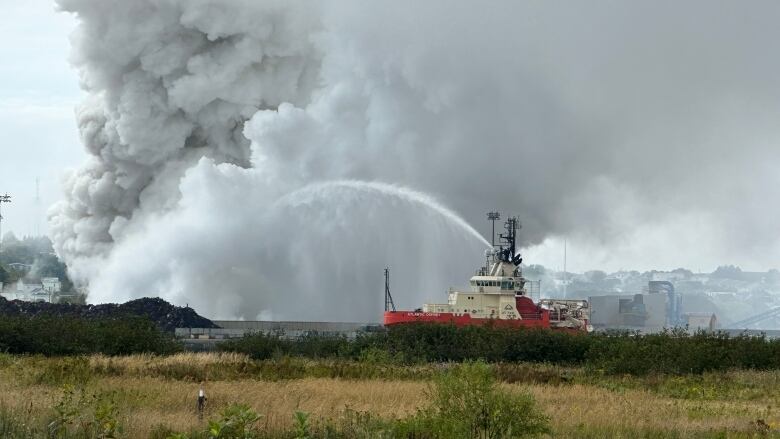 A barge pours liquid over large plumes of smoke