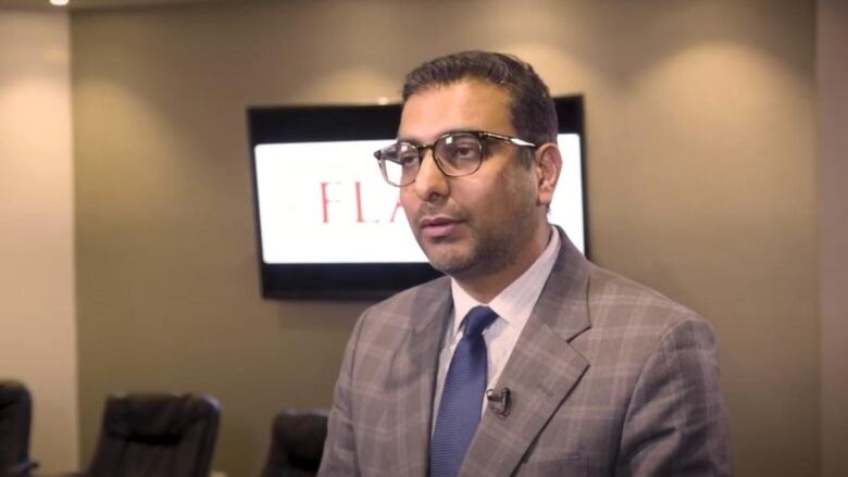 A man in a suit speaks to the camera in a board room.