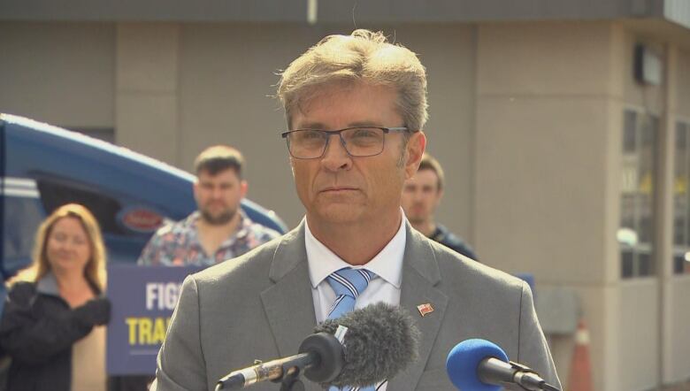 A politician in a grey suit speaks into a microphone at a campaign announcement.