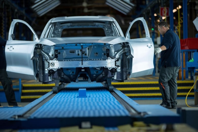 A worker at a Ford factory is shown inspecting the door of a Focus sedan.