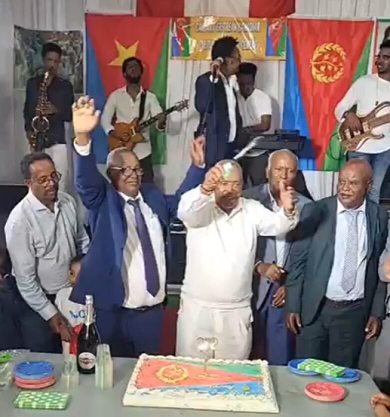 Men stand in front of a cake that has an image of the Eritrean flag. 