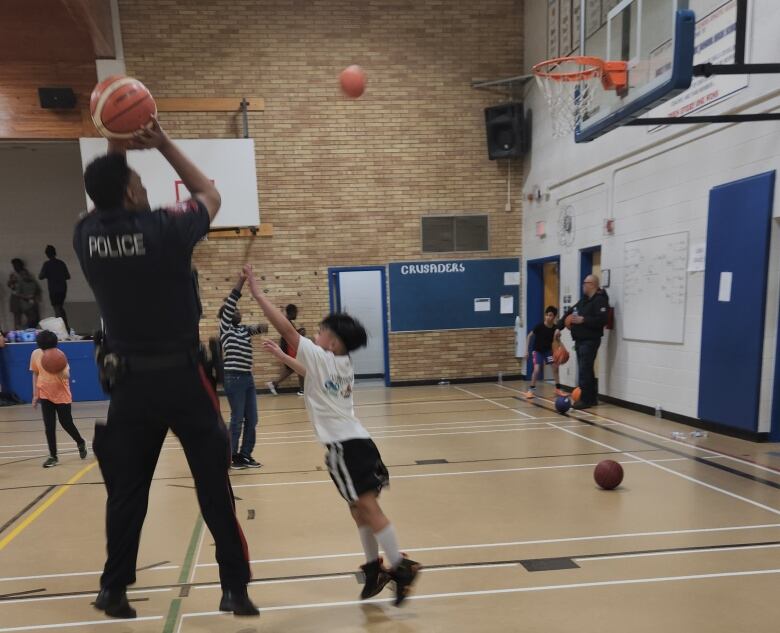 A man in a police uniform takes a shot on a basketball court.