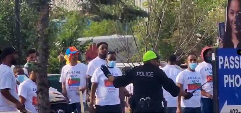 A police officer stands in front of a group of men wearing white t-shirts.