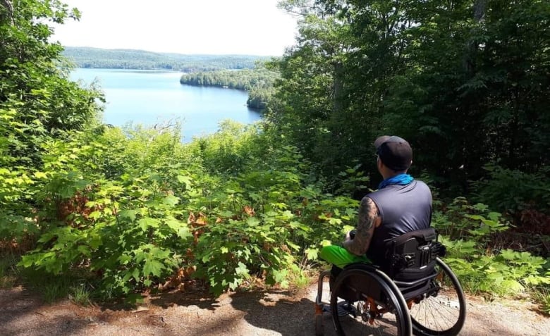 John Azlen sits in his wheelchair and looks out over a view of a lake. 