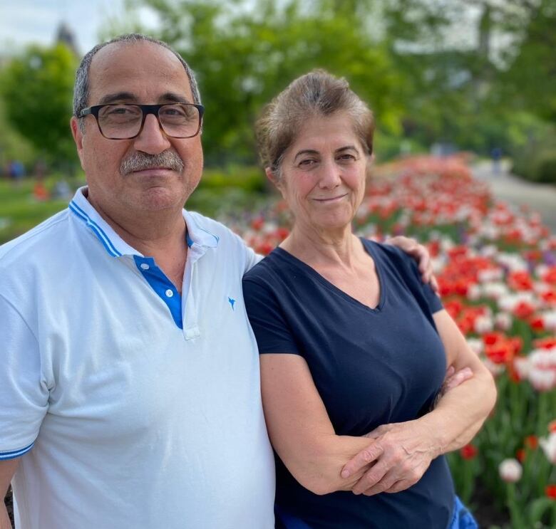 A man and a woman stand in front of flowers