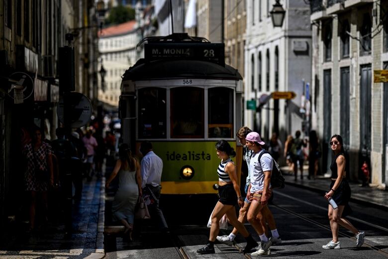 Several people cross a street in front of a tram.