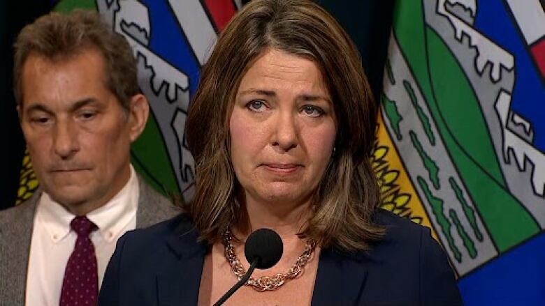 Alberta's premier is seen answering questions at a podium.