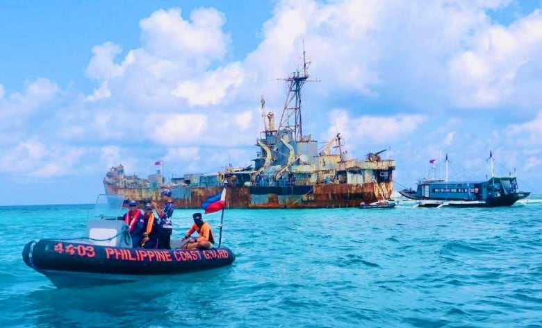 A Coast guard boat is seen on the water in the foreground, with a rusting ship in the background.