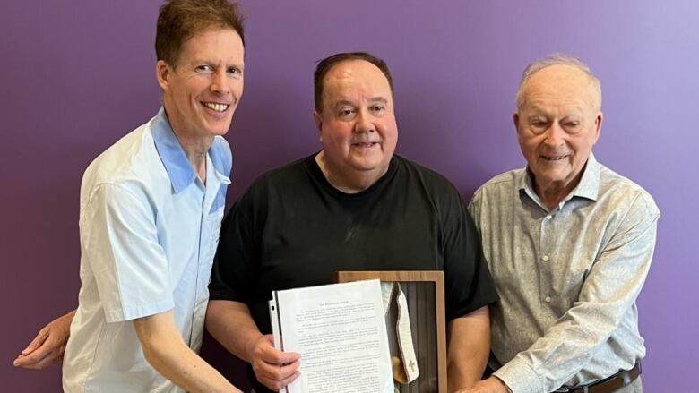 3 men smiling holding a plaque.