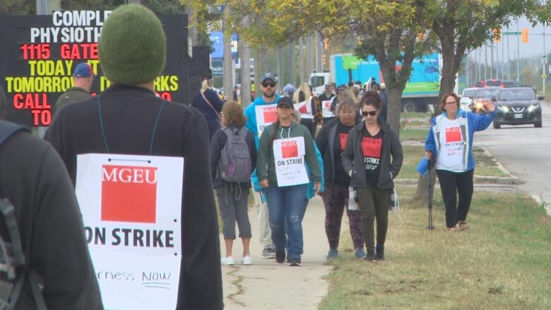 A group of people are seen picketing. One of them has a sign on his back that says 