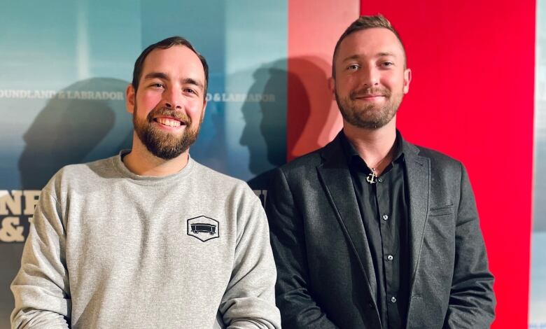 Two men smile in front of a CBC sign.