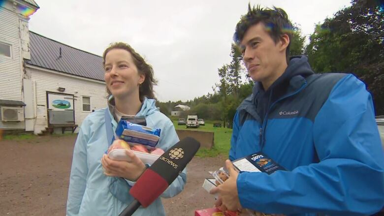 Two people standing outside holding food and speaking into a CBC-branded microphone