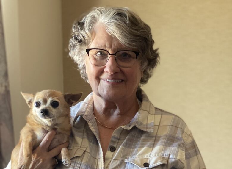 An elderly woman stands holding a chihuahua dog.