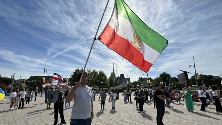 A man hoists the Iranian flag outside the National Gallery of Canada in Ottawa during a protest against the Iranian regime on Saturday. 