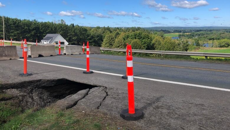 Orange pylons on a road near were the pavement is washed out. 