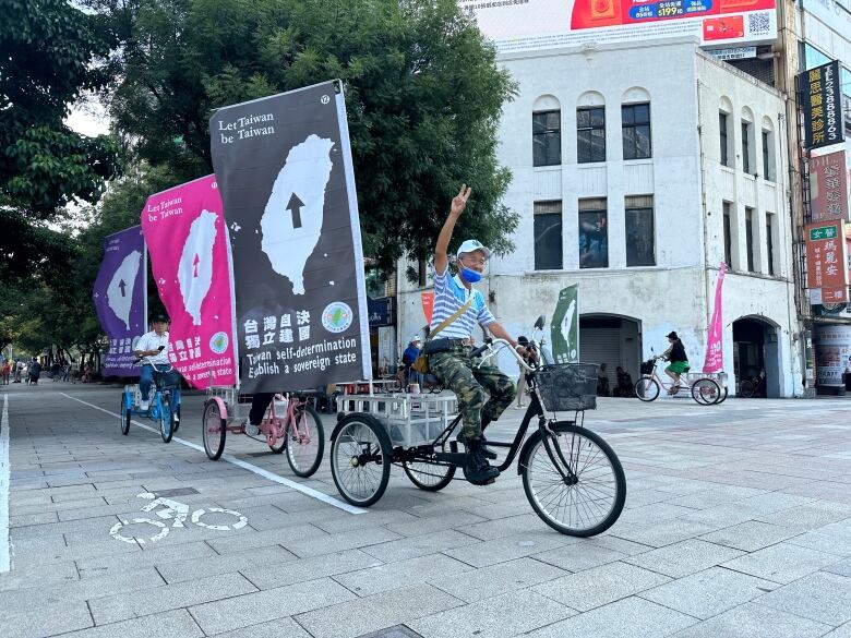 A person flashes the peace signs as they ride a tricycle adorned with a large flag.