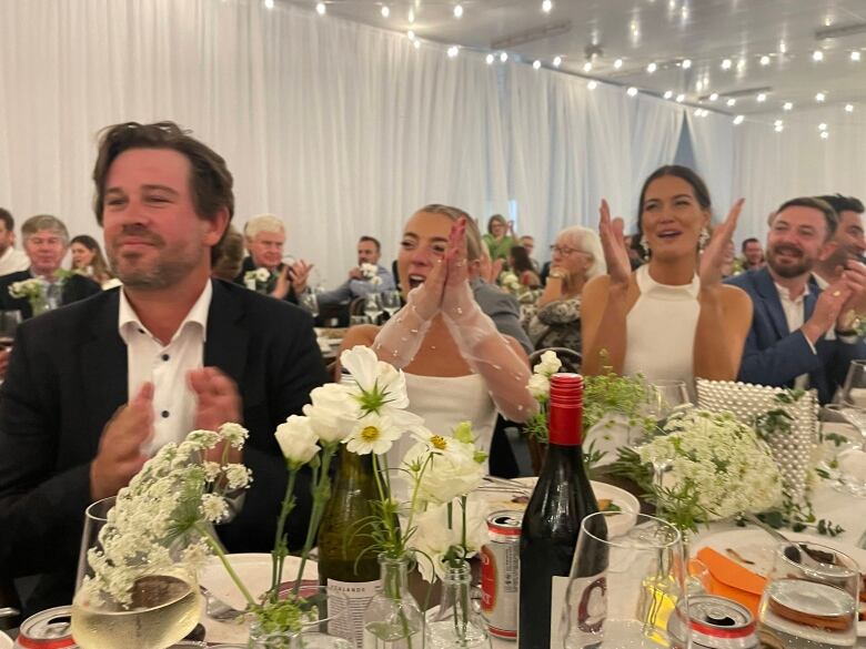 A wedding party clap as they sit at a decorated table.