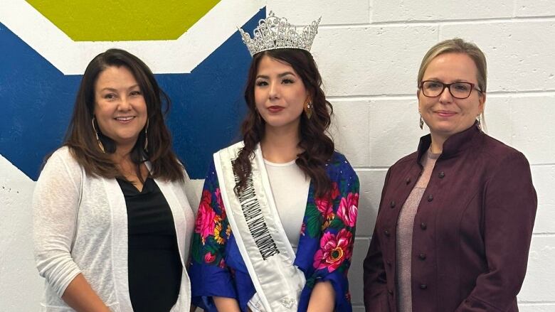 Three Cree women, including a young beauty Queen wearing a crown and a shash look into the camera.