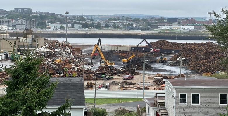 Heavy equipment on a waterfront industrial site with piles of scrap metal.