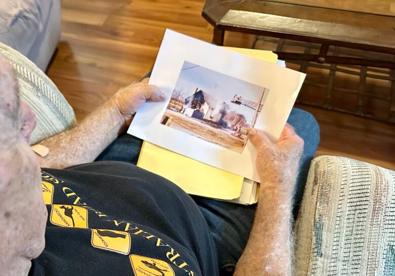 A senior-age man looks at a printed photo of a house fire.