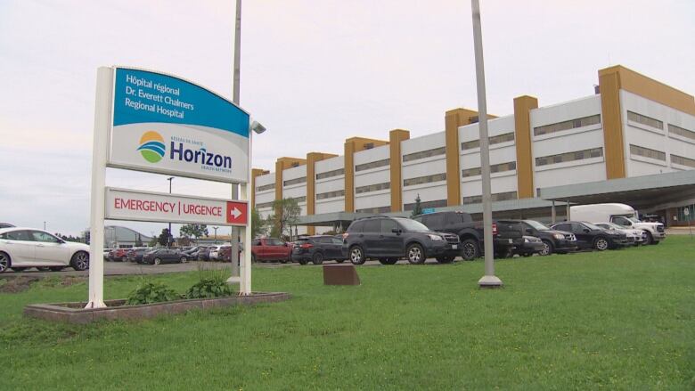 A large bilingual Horizon Health Network sign for the Dr. Everett Chalmers Regional Hospital and emergency department near the parking lot, with the building in the background.