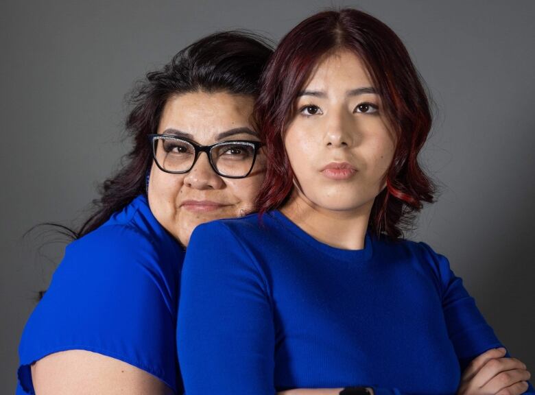 A Cree mother has her arms wrapped around her teenage daughter dressed in matching royal blue shirts.