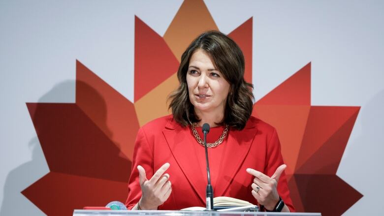 A woman wearing red with brown hair stands in front of Canadian flag.