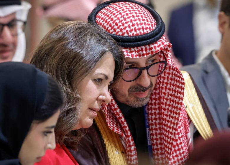 Two people lean their heads together to talk in the middle of a crowd.