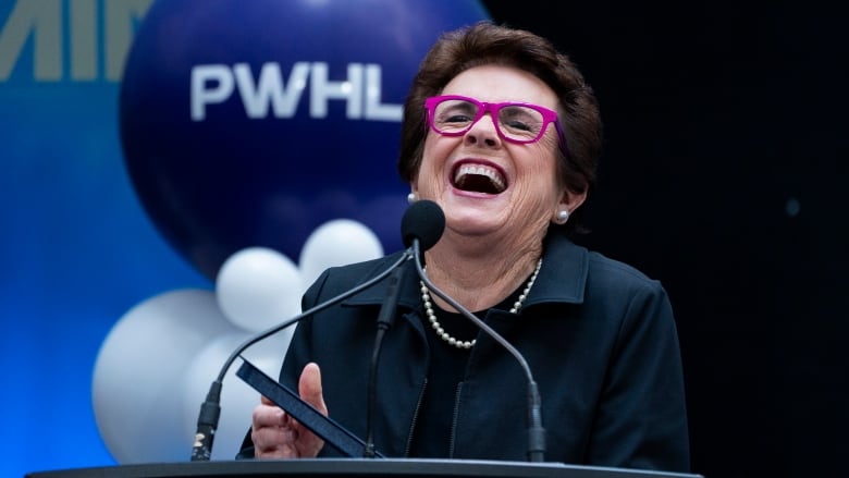 A former women's tennis player laughs while standing behind a podium.