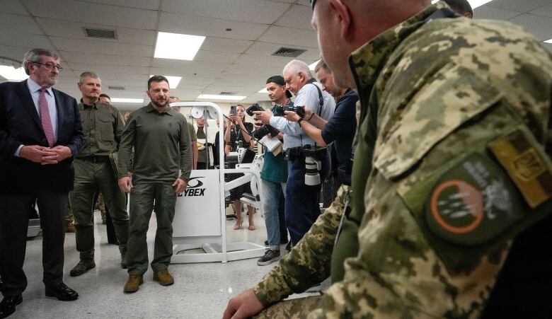 A man in military fatigues walks in front of reporters and other military personnel. 