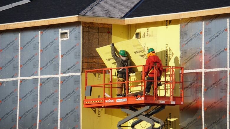 Some workers stand on a scissor lift, putting panels into place on an unfinished building