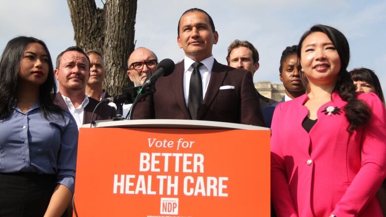 A man stands behind a podium with an orange sign.