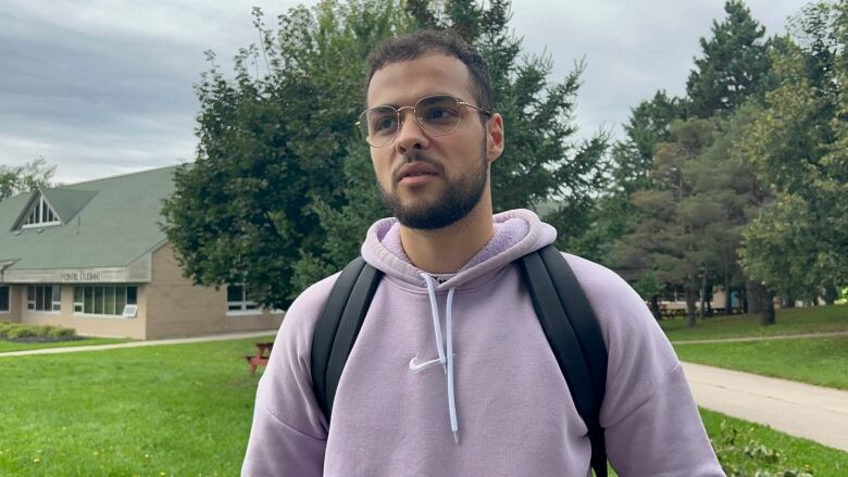 A Moroccon boy with glasses, short black hair, black trimmed beard. Wearing a purple hoodie and having a black backpack on his shoulders. 