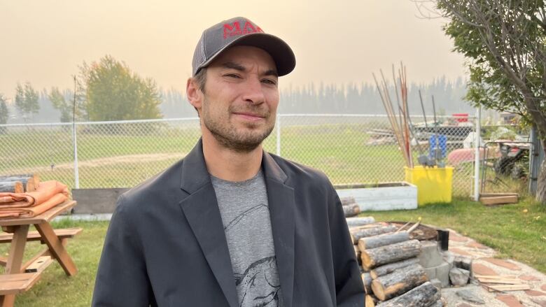 A man in a ball cap stands in a fenced yard.