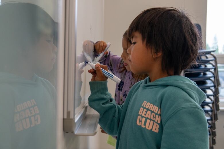 Two young children draw on a whiteboard.