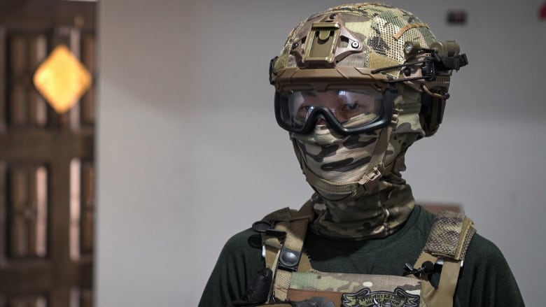 A person in full combat gear including a helmet is pictured. Only their eyes are visible through goggles.