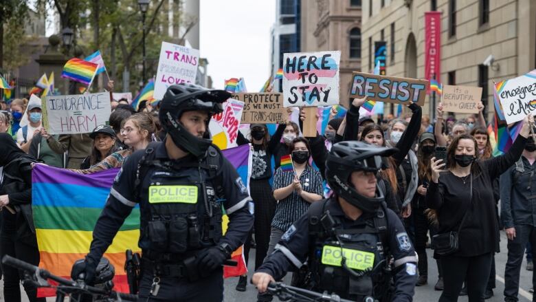 A group of people holding signs are shown in behind police officers.