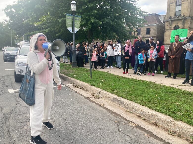 A woman in a bunny costume with a bullhorn and a crowd of people standing on the lawn next to her