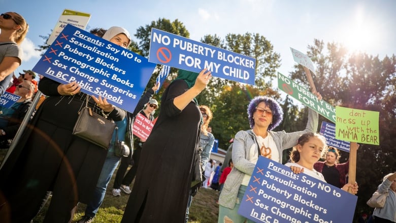 People hold up signs reading 'no puberty blockers for my child.'