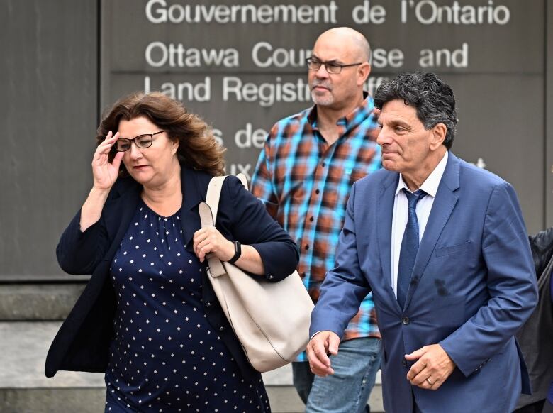 Three people walk past a sign for a provincial courthouse.