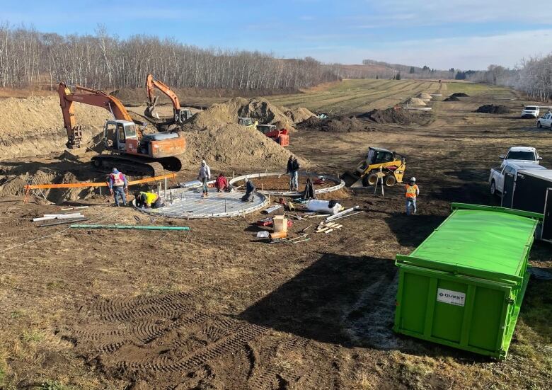 Brown dirt, a circle of grey concrete and two big orange excavators with workers dotting the construction project. 